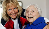 Foto: Pflegerin mit Seniorin - beide lachen.