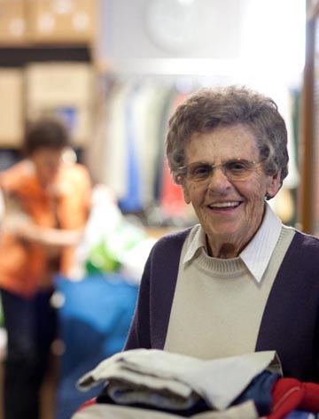 Foto: Eine ehrenamtliche Seniorin in der Kleiderkammer hält einen Stapel Kleidung und der Hand.