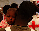 Foto: Ein haitianisches Baby schaut über die Schultern eines Rotkreuzhelfers.